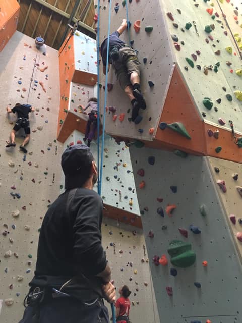 Indoor clmbing wall a person holds the rope for someone scaling the climbing wall