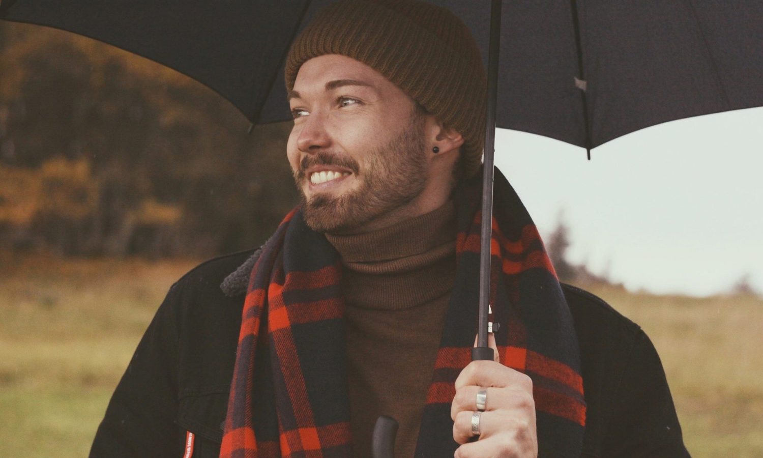 Happy, smiling man holding an umbrella smiling off camera wearing a scarf and wooly hat