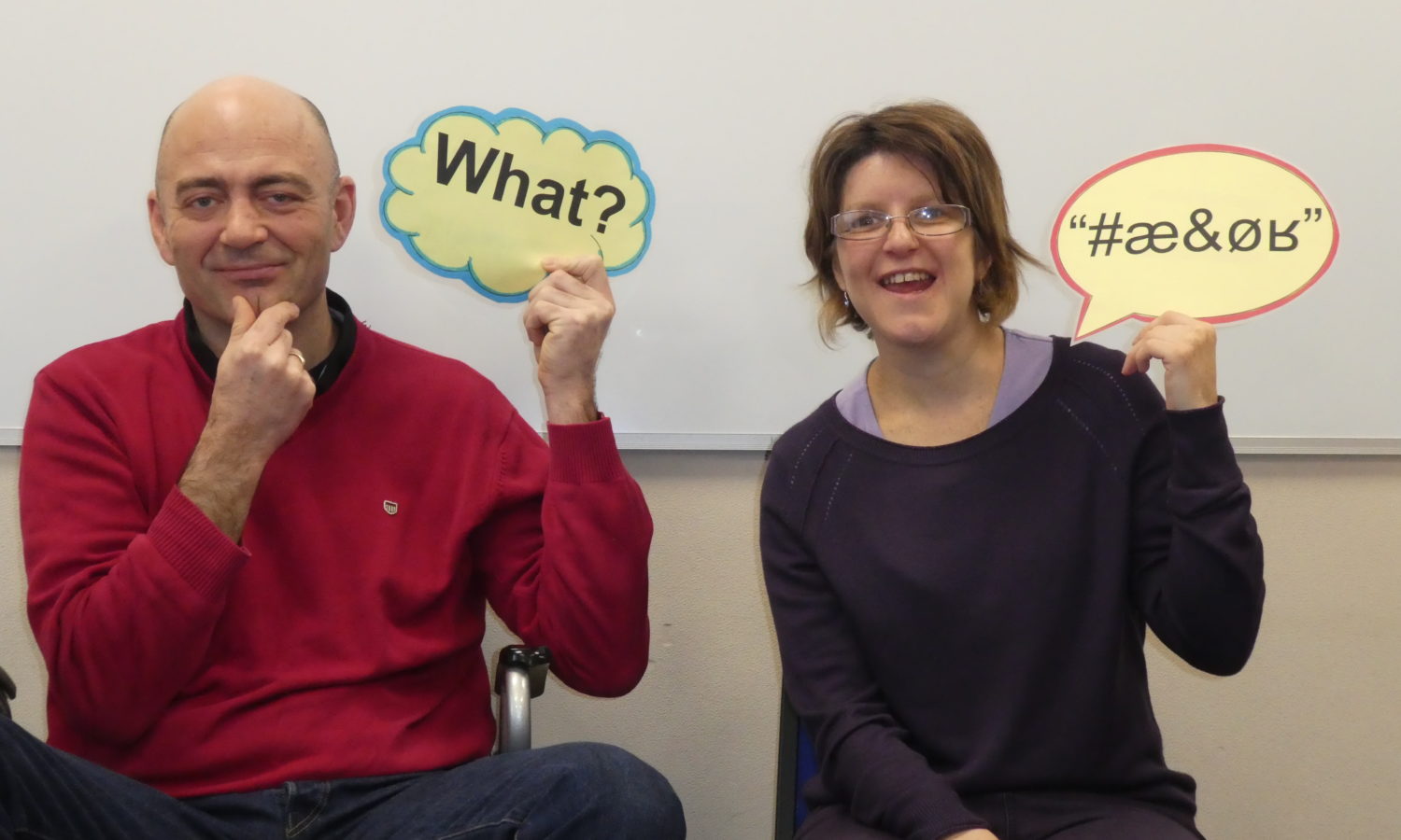 Two people one hold up a speech bubble that says 'What?' and another holding a speech bubble with confused graphics