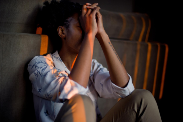 Woman sat in the dark with stripes of orange light coming through the window on her. She has her head in her hands, lonely and sad