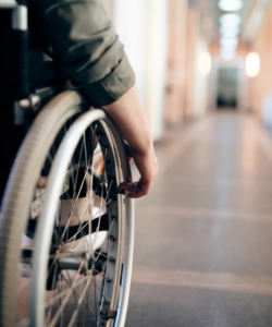 left hand image we see the side of a person in a wheelchair wheeling down a well lit corridor, looks like a health care establishment.