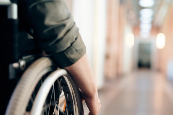 left hand image we see the side of a person in a wheelchair wheeling down a well lit corridor, looks like a health care establishment.