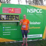 A female runner holding her medal after completing a running race, raising funds for Living Options Devon