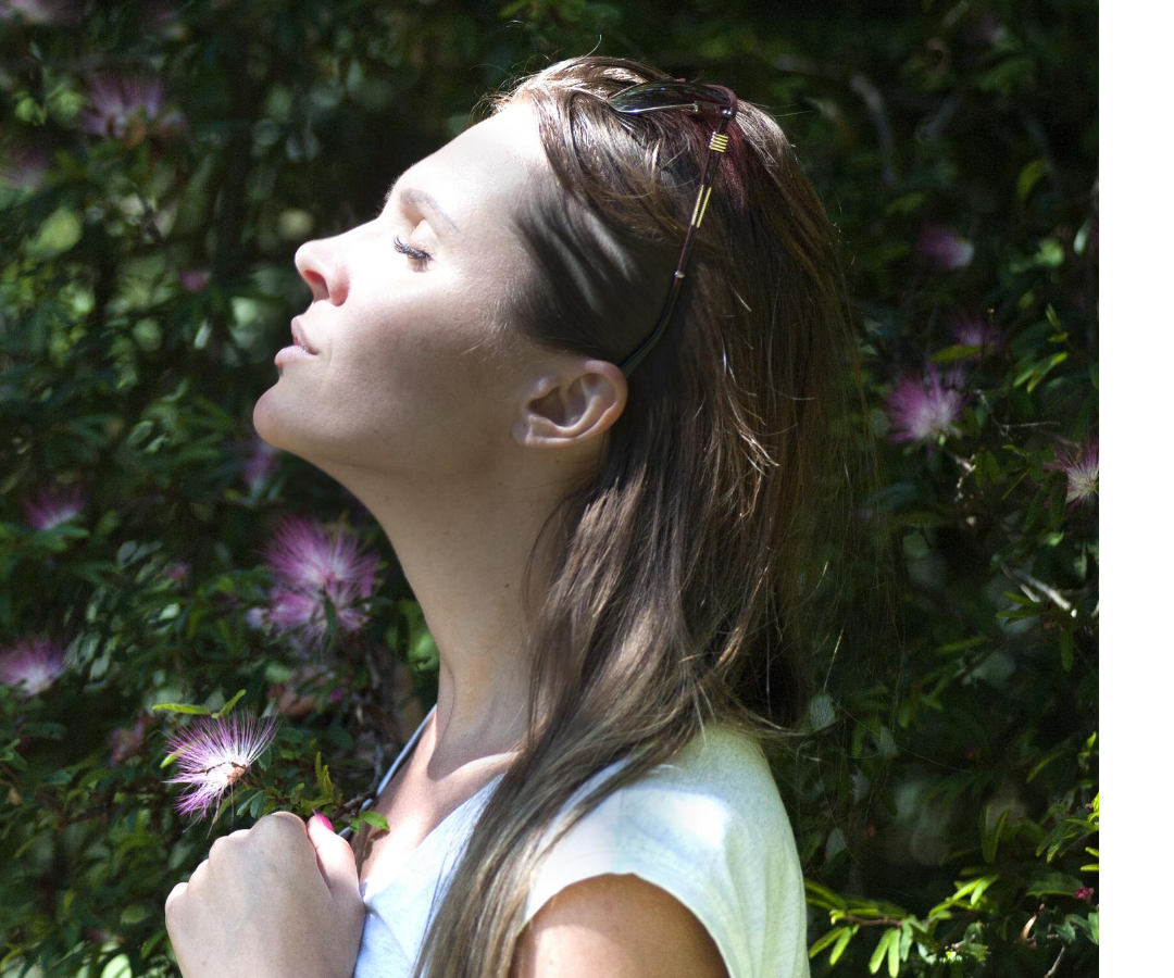 A woman side ways on in a garden, with her face lifted to the sun, eyes closed.