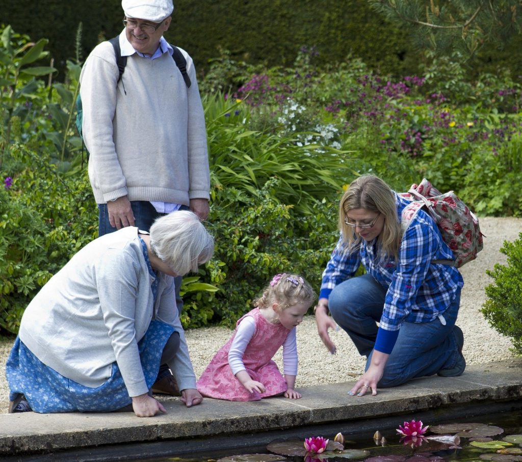 Grandparents in a garden with thier grand daughter and her mother look into a garden pond.