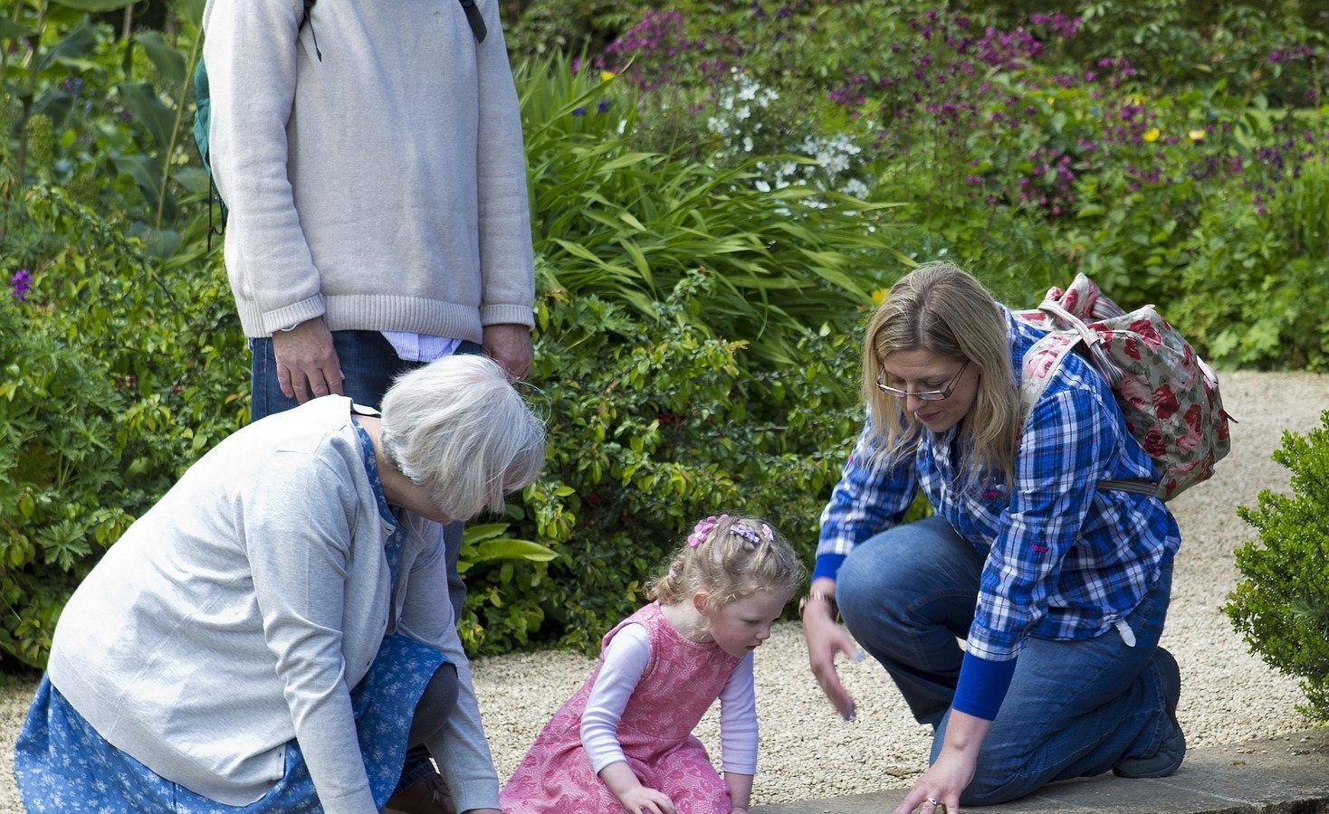 Grandparents in a garden with thier grand daughter and her mother look into a garden pond.