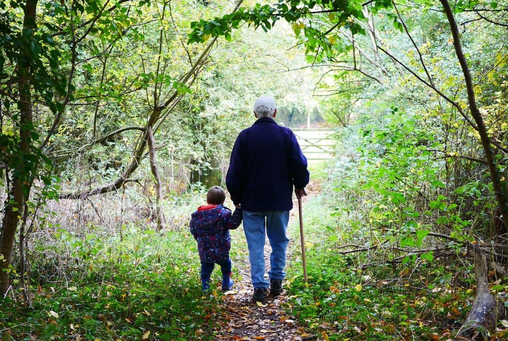 Elderly man with walking stick walking with grandchild outside in the countryside