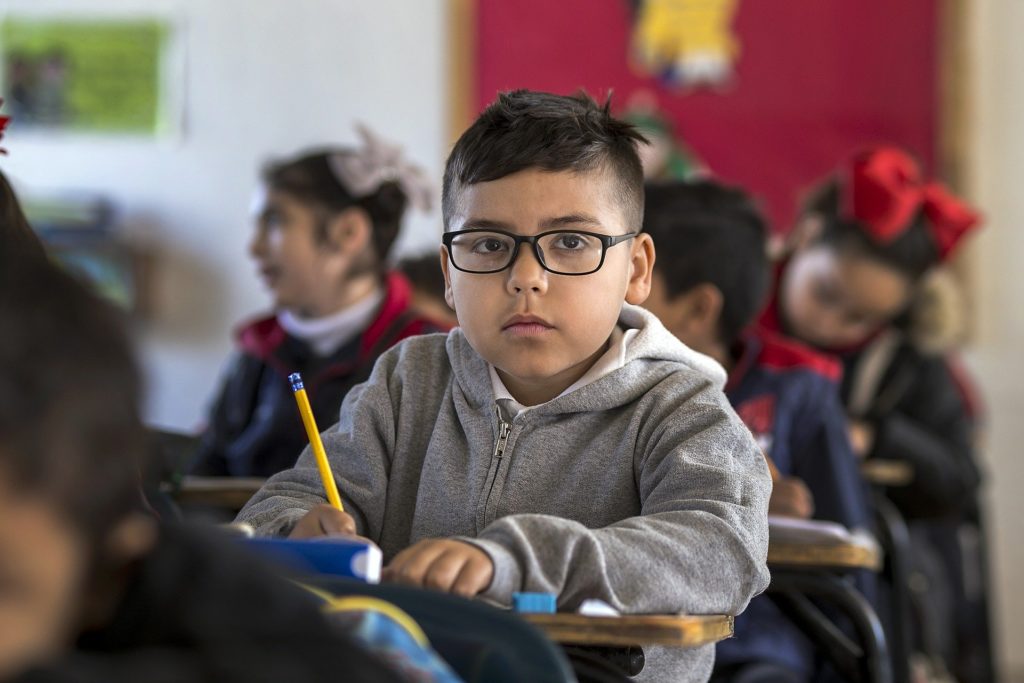 Boy wearing classrooms in the classroom sat at his desk holding his pencil.