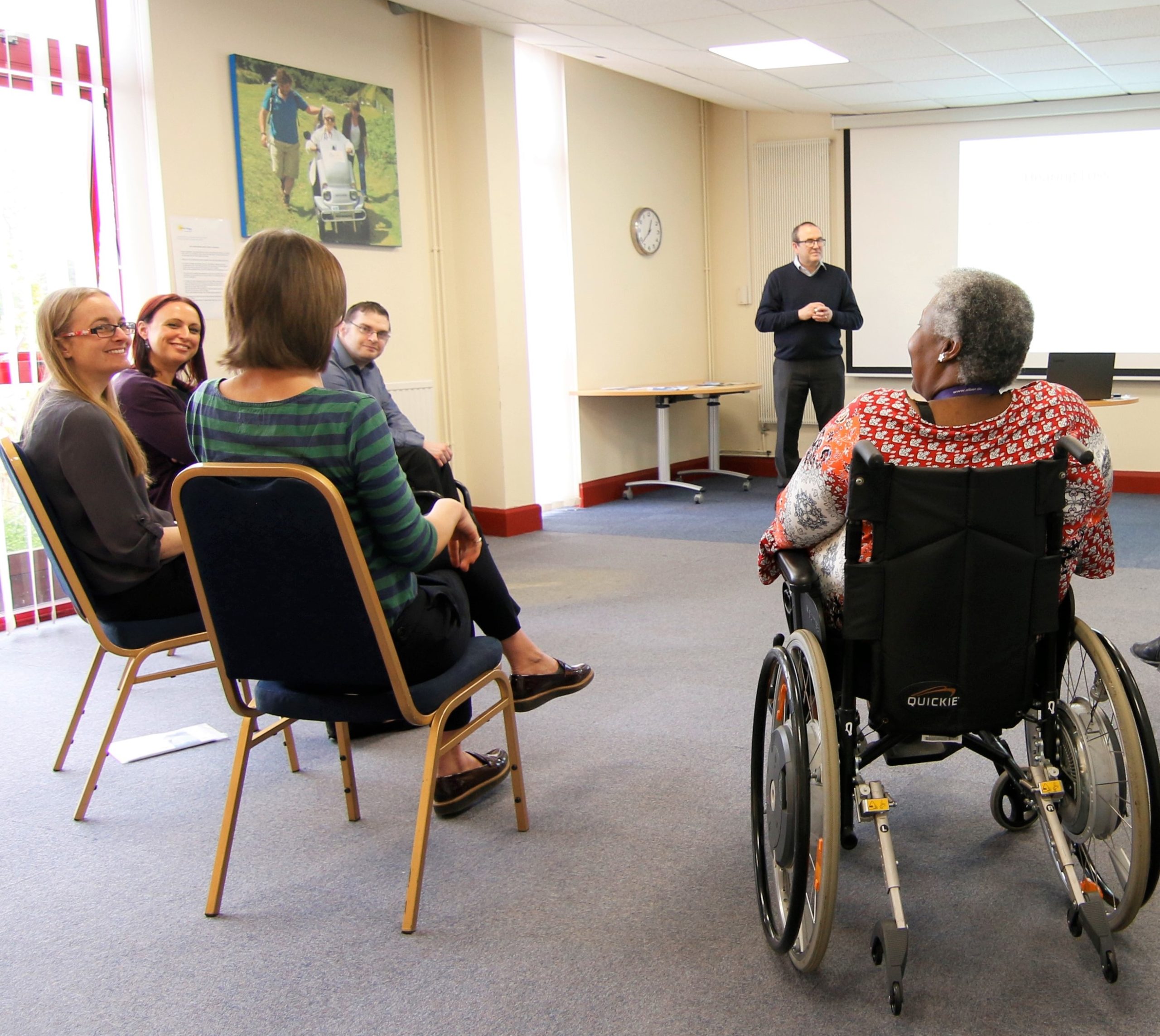 a group of people in the LOD office during a training or workshop session. The people are chatting and smiling, one of the females is a wheelchair user.