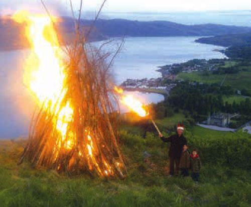 Man and two children standing next to their fire beacon that they have just lit