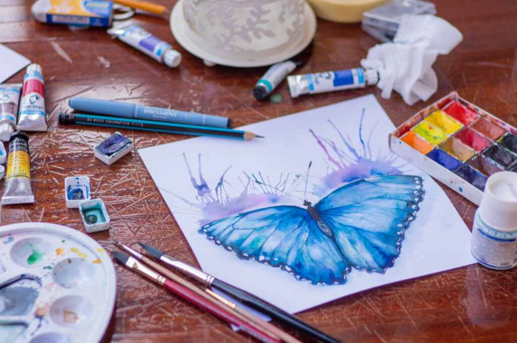 Illustration of a butterfly on an artists bench with brushes and paints spread around