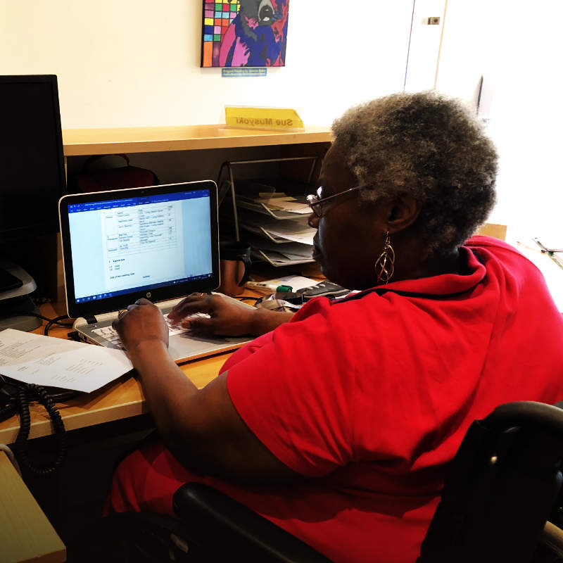 a female wheelchair user working on a laptop at an office desk