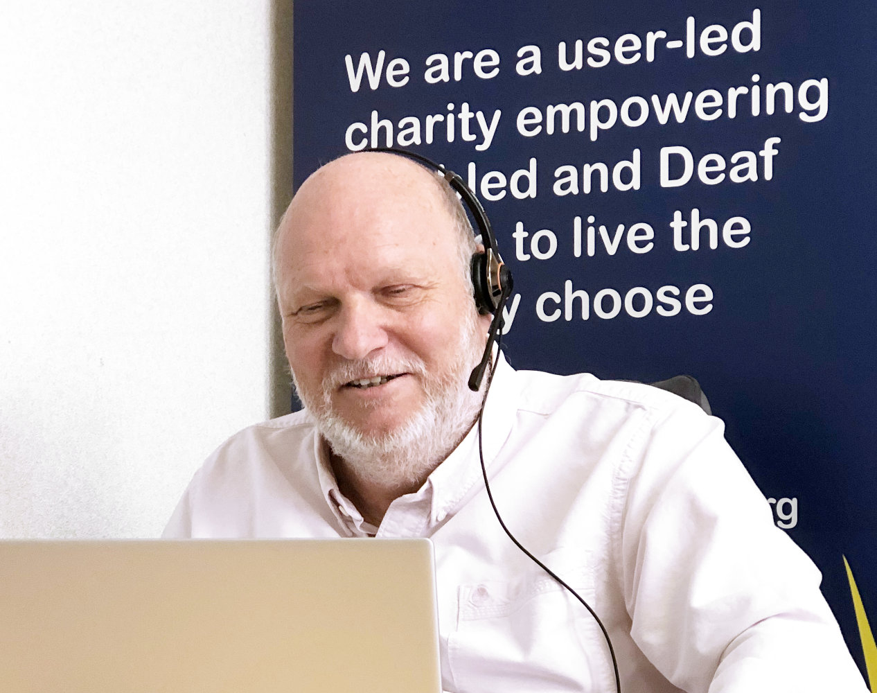 Home from Hospital call handler with headset and laptop sitting in front of a banner saying We are a user-led charity empowering disabled and Deaf people to live the life they choose