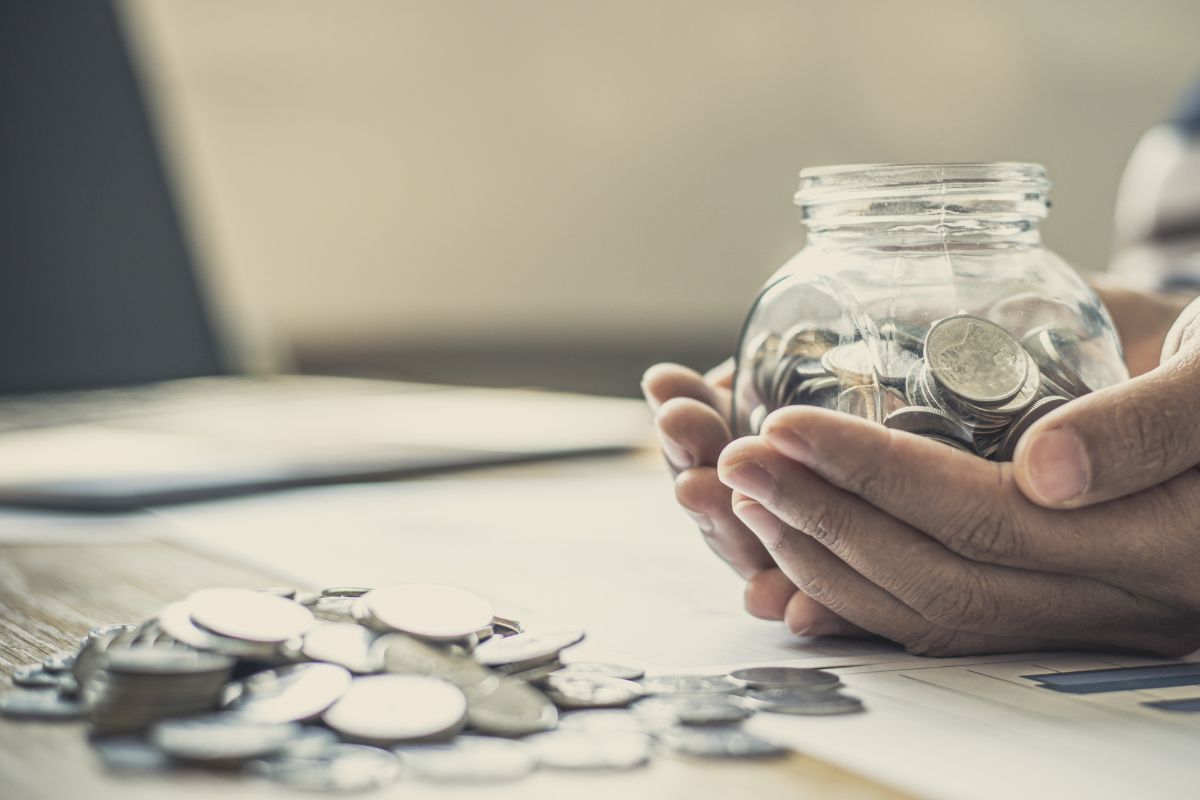 Coins on a table and held in a clear container by a pair of hands