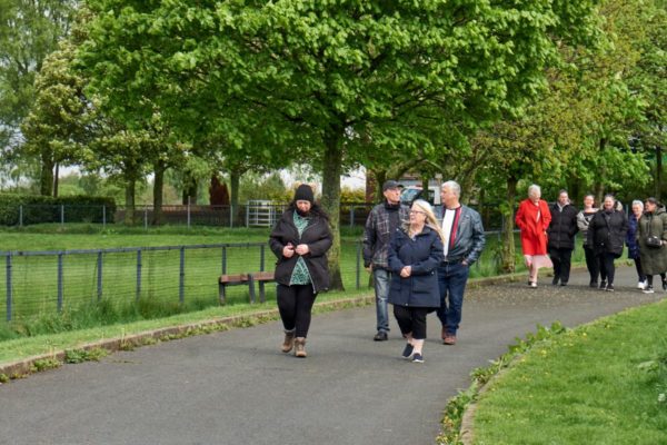 A mixed group of people walking along a path in a park surrounded by trees
