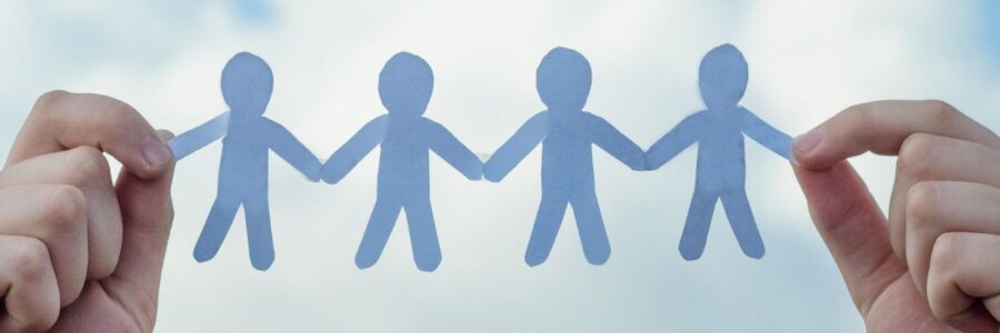 A paperchain of people being held between two hands against a bright blue sky with white clouds