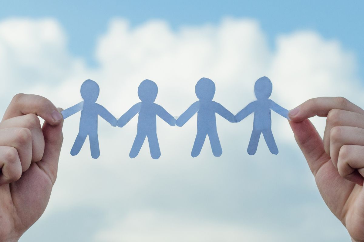 A paperchain of people being held between two hands against a bright blue sky with white clouds