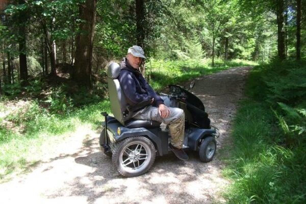 A countrside mobility member sits on a tramper surrounded by woodland as the sun shines
