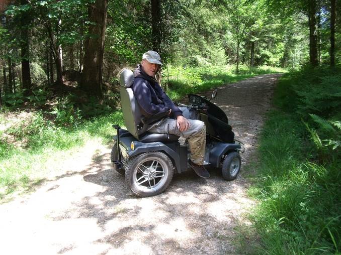 A countrside mobility member sits on a tramper surrounded by woodland as the sun shines
