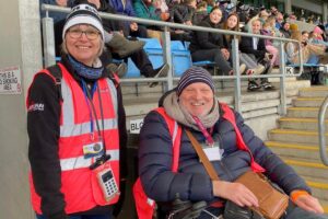 Two of the LOD team stand in high vis tabards bucket collecting on match day