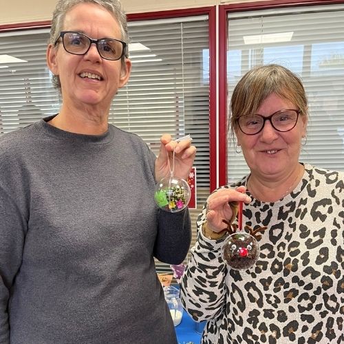 Two crafters hold up their christmas bauble creations