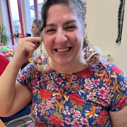 A crafter smiles at the camera wearing handmade baubles as earings