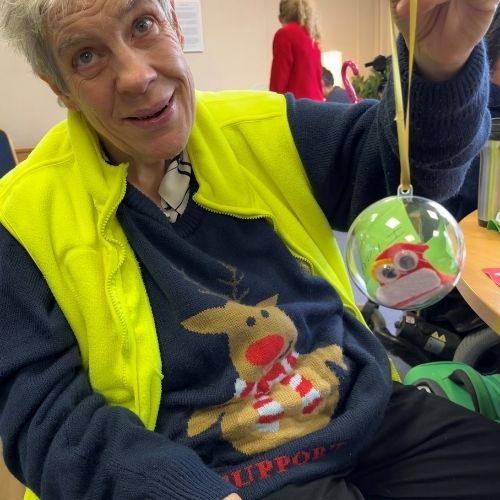 A bauble is held up to the camera by a lady in a reindeer christmas jumper  