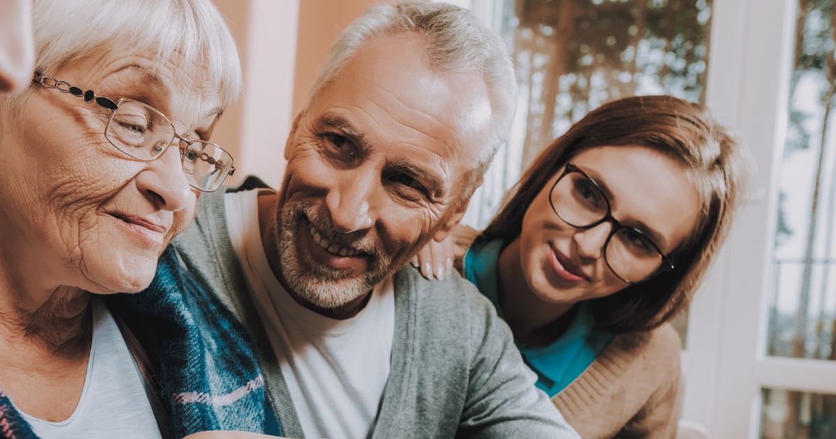 Three adults of different ages sit together as the oldest person looks ahead smiling