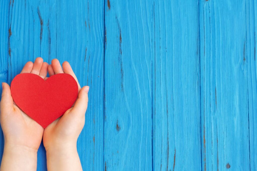 An open set of hands hold a red piece of heart-shaped card