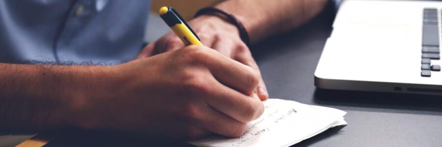 A hand holding a pen writes on a piece of paper