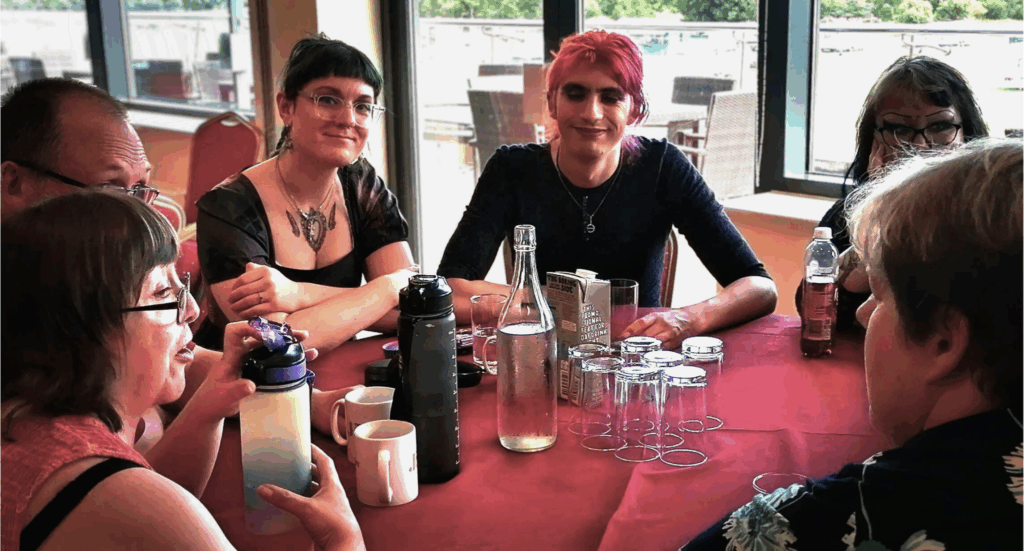 Some of our Oliver McGowan team are sat around a table at the event. Some are in conversation, while others are smiling at the camera.